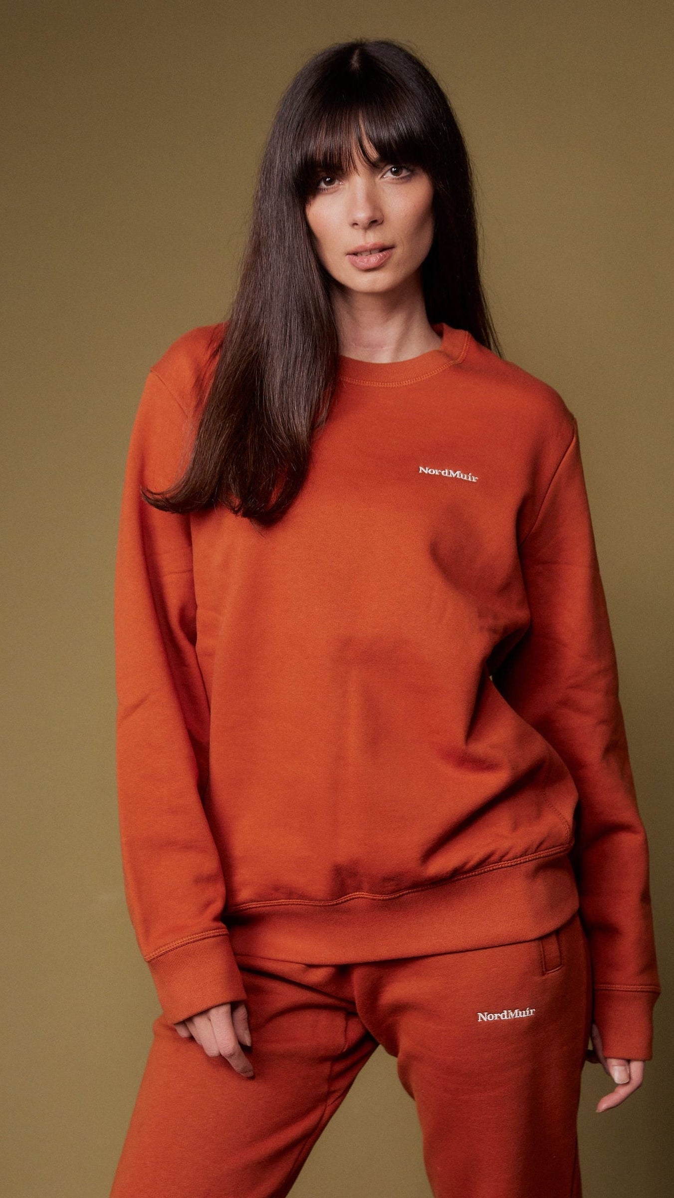 Person wearing a red sweatshirt and pants against a brown background