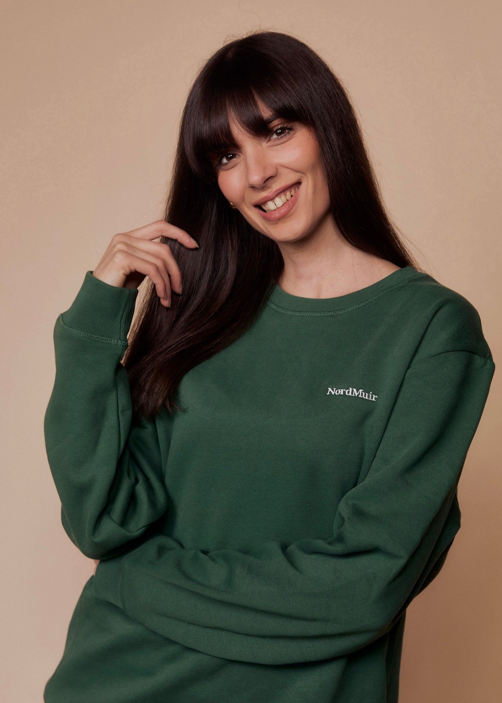 Woman wearing a green sweatshirt with 'NordMuir' logo against a beige background